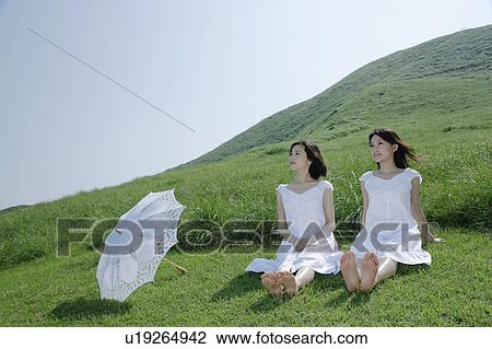 Stock Image - Two young women sitting on grass field. Fotosearch