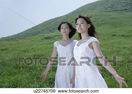 Two young women standing in field View Large Photo Image Stock Photo - Two young women standing in field. Fotosearch