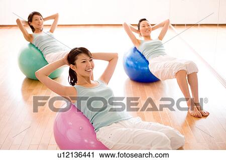 Stock Image - Young women lying on fitness balls doing sit-ups. Fotosearch