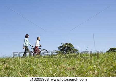 Two young women walking, one pushing bicycle View Large Photo Image Stock Photo - Two young women walking, one pushing bicycle. Fotosearch