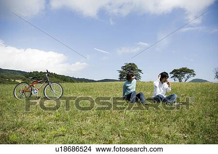Picture - Young couple sitting on field, man using mobile phone. Fotosearch
