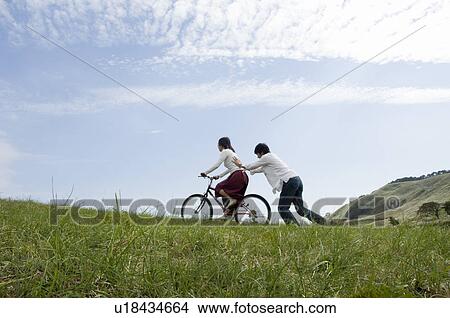 Picture - Young man pushing young woman on bicycle. Fotosearch