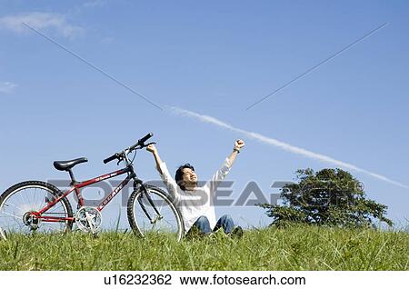 Young man sitting next to bicycle, arms outstretched View Large Photo Image Stock Image - Young man sitting next to bicycle, arms outstretched. Fotosearch