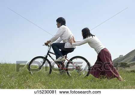 Young woman pushing young man on bicycle View Large Photo Image Stock Image - Young woman pushing young man on bicycle. Fotosearch