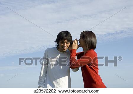 Stock Image - Young woman whispering to young man. Fotosearch