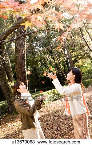 Two young women catching falling leaves View Large Photo Image Stock Photo - Two young women catching falling leaves. Fotosearch