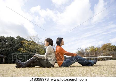 Two young women sitting on lawn back to back View Large Photo Image Stock Image - Two young women sitting on lawn back to back. Fotosearch