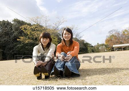 Two young women sitting on lawn looking at camera View Large Photo Image Stock Photography - Two young women sitting on lawn looking at camera. Fotosearch