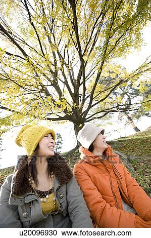 Stock Image - Two young women sitting on riverbank. Fotosearch