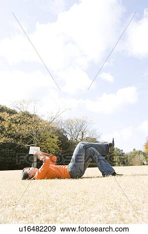 Young woman lying down on lawn reading View Large Photo Image Stock Photo - Young woman lying down on lawn reading. Fotosearch