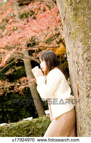 Stock Image - Young woman standing under tree. Fotosearch