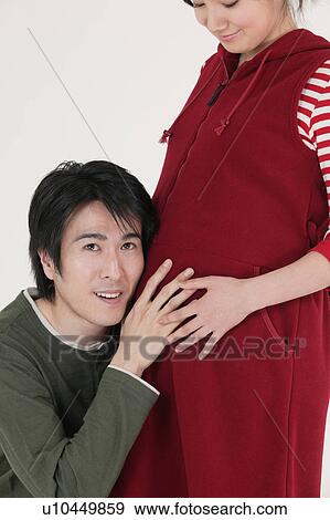 Stock Photo - Husband holding ear to his wife's stomach. Fotosearch