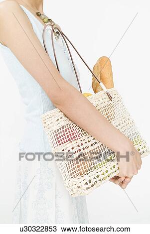 Stock Image - Young woman holding bag, midsection. Fotosearch