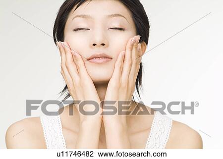 Young woman touching her cheeks View Large Photo Image Stock Image - Young woman touching her cheeks. Fotosearch
