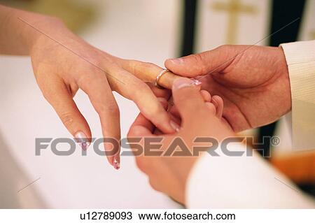 Stock Image - Groom placing wedding ring on bride's finger . Fotosearch