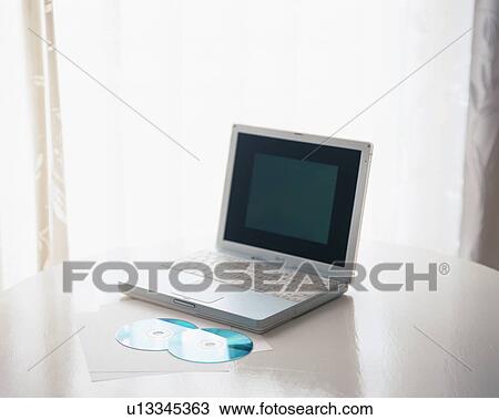 Stock Image - A laptop pc with two compact discs on table. Fotosearch
