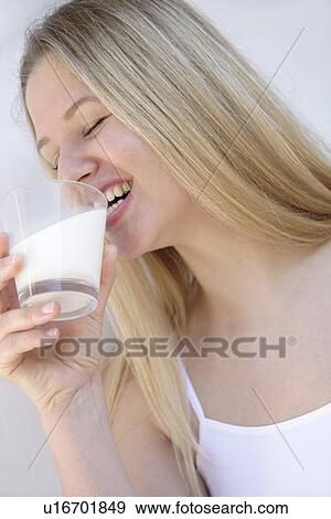 Stock Photo - Young blond woman drinking glass of milk, laughing, close up. Fotosearch
