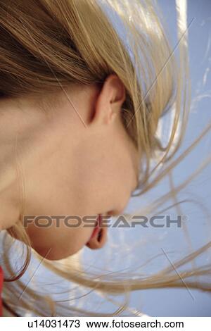 Stock Image - Young woman throwing her long blond hair in front of blue sky, low angle view. Fotosearch