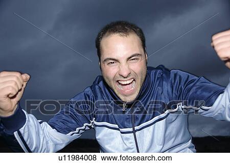 Young man in a sweat suit jacket cheering in front of dark clouds View Large Photo Image Stock Photo - Young man in a sweat suit jacket cheering in front of dark clouds. Fotosearch
