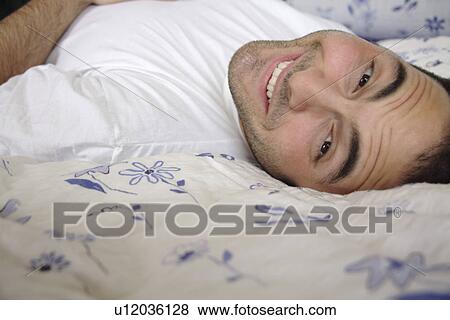 Young man lying in bed, smiling and relaxing View Large Photo Image Stock Photo - Young man lying in bed, smiling and relaxing. Fotosearch