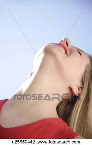 Stock Image - Young woman in a happy mood in front of blue sky, view from below. Fotosearch