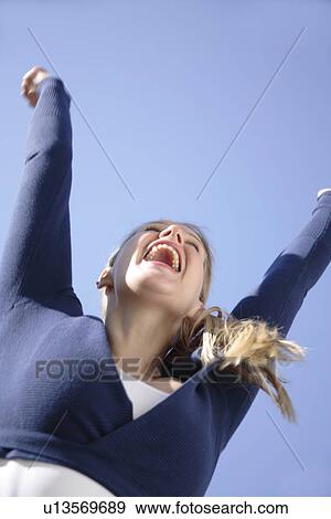 Stock Photo - Young woman jumping happily in front of blue sky, view from below. Fotosearch