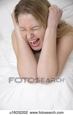Stock Image - Young woman sitting in bed, screaming. Fotosearch