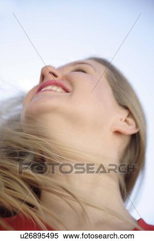 Stock Photography - Young woman tossing her long blond hair in front of blue sky, view from below. Fotosearch