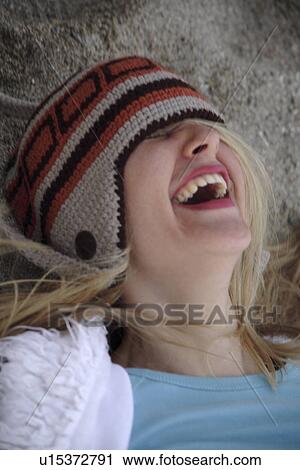 Stock Image - Young woman wearing knitted cap, lying in the sand at the beach, laughing, close up. Fotosearch