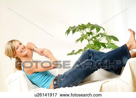 Stock Photo - Woman relaxing on sofa, feet on arm-rest. Fotosearch