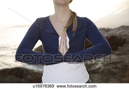 Stock Photo - Woman standing at a rocky sea coast, meditating. Fotosearch
