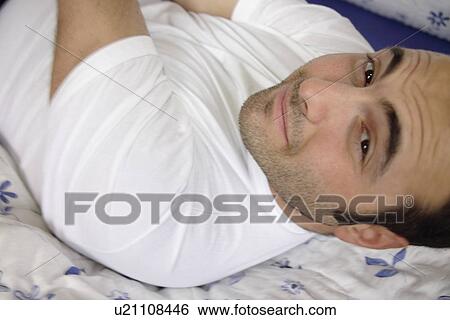 Stock Photograph - Young man lying in bed, smiling. Fotosearch