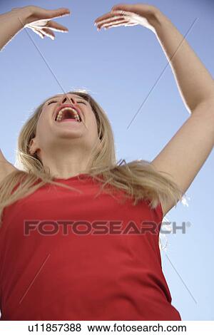 Young woman dancing and cheering with arms stretched out in front of blue sky, low angle view View Large Photo Image Stock Photo - Young woman dancing and cheering with arms stretched out in front of blue sky, low angle view. Fotosearch