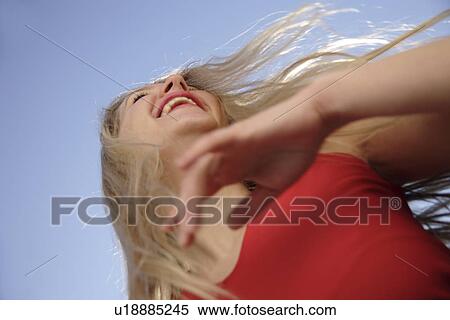 Stock Photography - Young woman with arms stretched out in front of blue sky, low angle view. Fotosearch