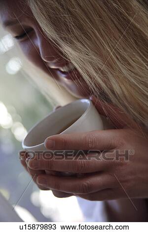 Stock Image - Woman in bathrobe drinking cup of tea, close up. Fotosearch