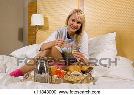 Stock Image - Young girl having breakfast in bed in her pajamas. Fotosearch