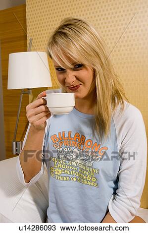 Stock Image - Young girl having breakfast in bed in her pajamas. Fotosearch
