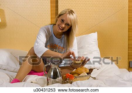 Stock Image - Young girl having breakfast in bed in her pajamas. Fotosearch
