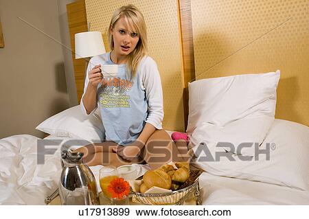 Stock Photo - Young girl having breakfast in bed in her pajamas. Fotosearch
