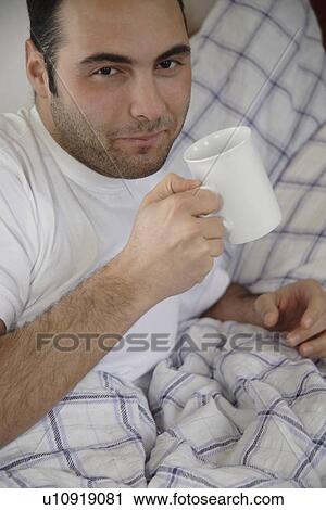 Young man drinking coffee in bed View Large Photo Image Stock Image - Young man drinking coffee in bed. Fotosearch