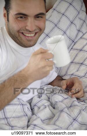 Young man drinking coffee in bed View Large Photo Image Stock Image - Young man drinking coffee in bed. Fotosearch