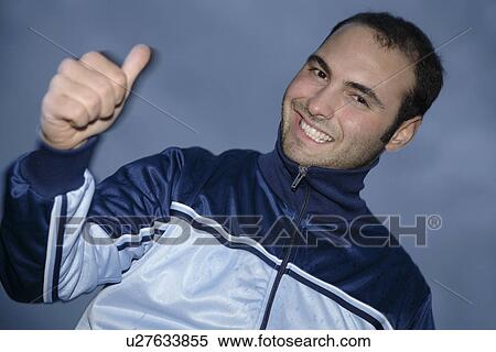 Stock Photography - Young man in a sweat suit jacket cheering in front of dark clouds. Fotosearch