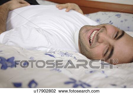 Young man lying in bed, smiling and relaxing View Large Photo Image Stock Image - Young man lying in bed, smiling and relaxing. Fotosearch