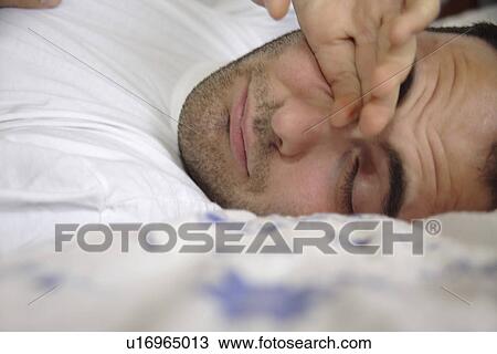 Young man lying in bed, waking up, rubbing his eyes, close up View Large Photo Image Stock Image - Young man lying in bed, waking up, rubbing his eyes, close up. Fotosearch