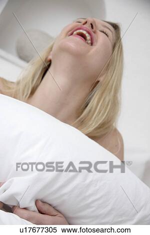 Young woman in bed, holding a pillow and laughing View Large Photo Image Stock Photography - Young woman in bed, holding a pillow and laughing. Fotosearch