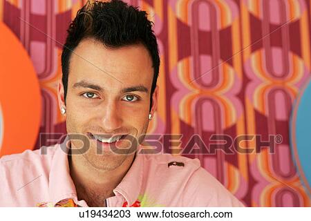 Stock Image - Young man sitting front of seventies style wallpaper, portrait. Fotosearch