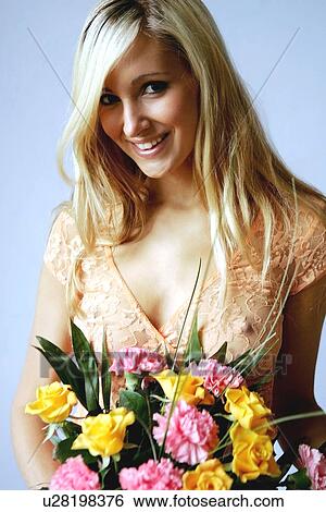 Stock Photograph - Young woman in see-through top holding bouquet of flowers, smiling. Fotosearch