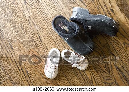 Stock Image - Black slippers and baby sneakers on hardwood floor. Fotosearch