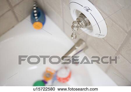 Stock Image - Detail of bathtub faucet with baby toys in the background, close up. Fotosearch