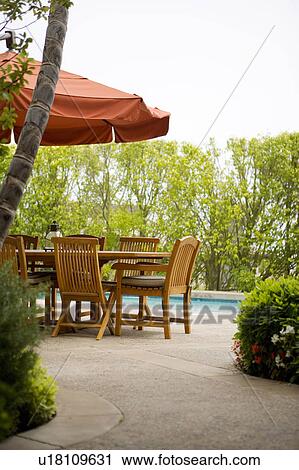 Stock Image - Detail of sitting area by pool covered with red umbrella. Fotosearch